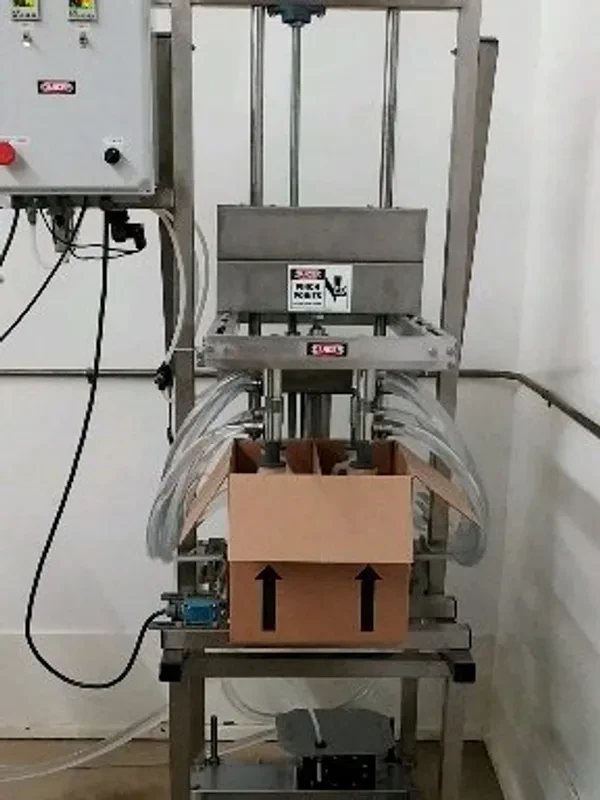 Four-head in-case overflow filling machine filling gallon bottles inside a cardboard box